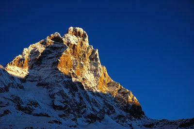 Low angle view of snowcapped mountain against clear blue sky