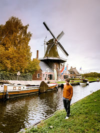 Portrait of man with hands in pockets standing by canal against sky