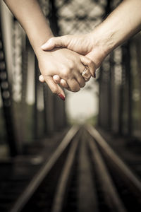 Cropped image of couple holding hands over railroad tracks