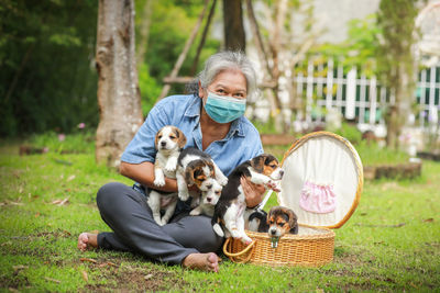 Senior woman wearing mask holding puppies sitting outdoors