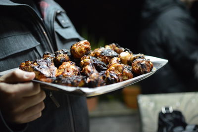 Close-up of hand holding grilled meat in plate