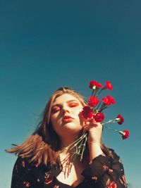 Portrait of young woman with red flowers against blue sky