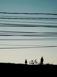 Silhouette people riding bicycle on field against sky