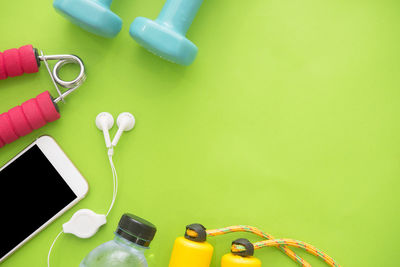 Directly above shot of mobile phone with exercise equipment over green background