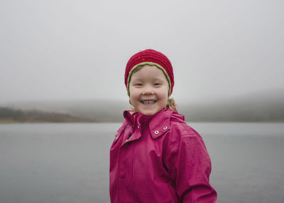 Portrait of happy girl standing by lake against sky during foggy weather