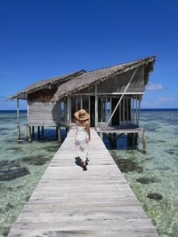 Full length of woman walking on pier over sea against blue sky