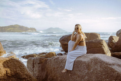 Rear view of woman sitting on rock at beach