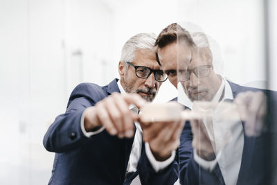 Two businessmen examining architectural model at glass pane