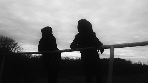 Silhouette friends standing by railing against sky