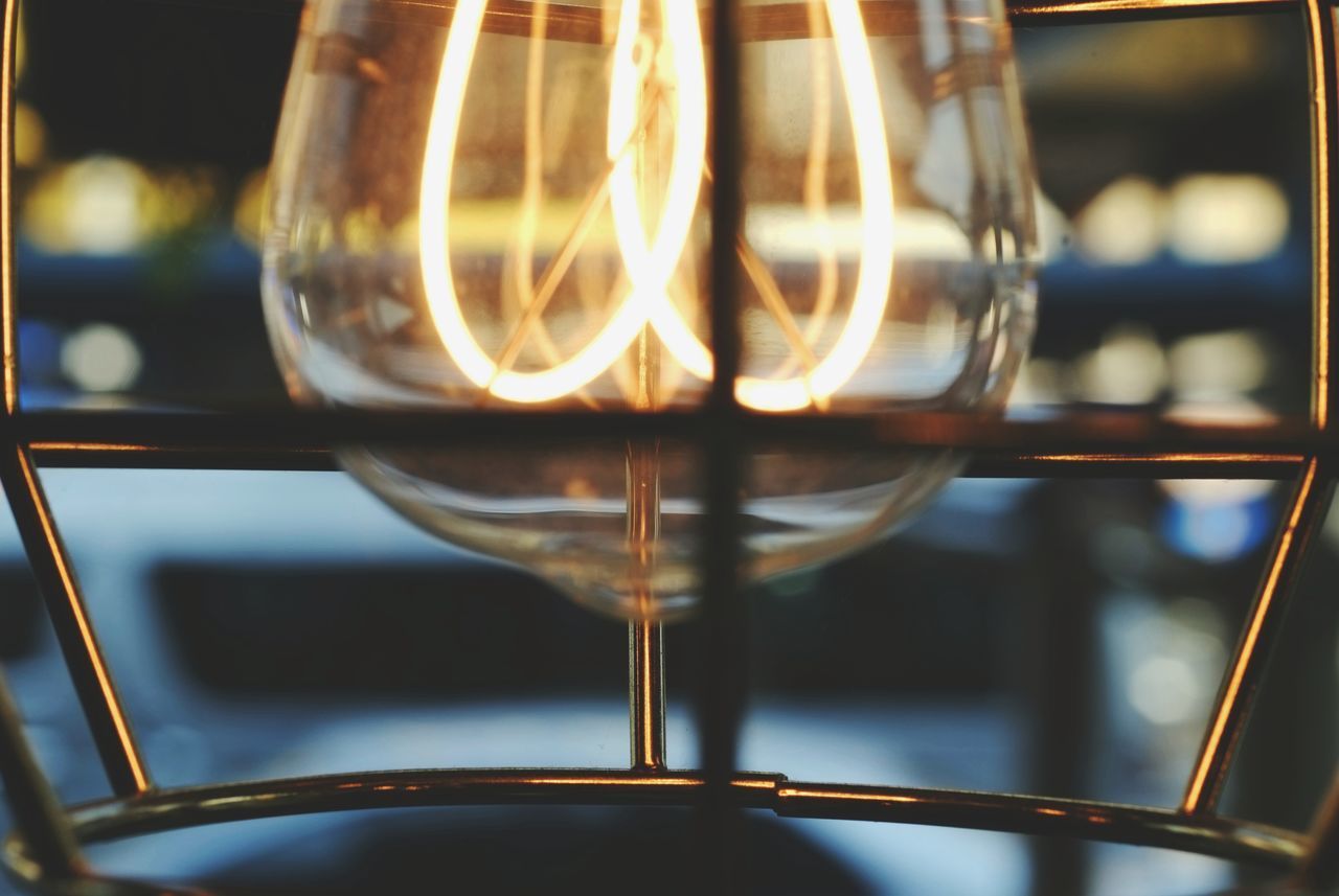 CLOSE-UP OF ILLUMINATED LIGHT BULB AGAINST WINDOW