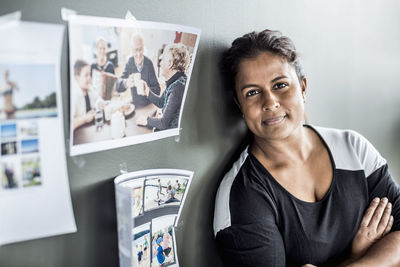 Portrait of businesswoman with arms crossed leaning on wall in office