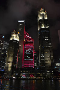 Illuminated buildings by river against sky at night