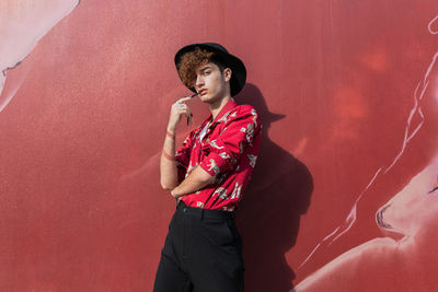 Young vain man in stylish wear standing on tiled walkway while looking at camera on street