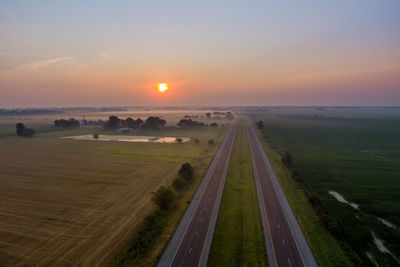 Panoramic view of road amidst field against sky during sunset