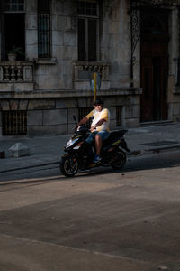 Side view of man riding motor scooter on street