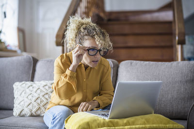 Young woman using laptop while sitting on sofa at home