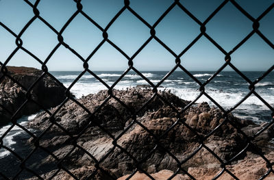 Scenic view of sea seen through chainlink fence