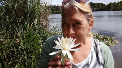 Close-up portrait of woman smelling flower at lake