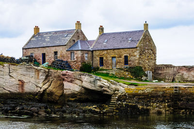 Old houses by river against sky