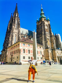 Rear view of woman standing by historic building against blue sky