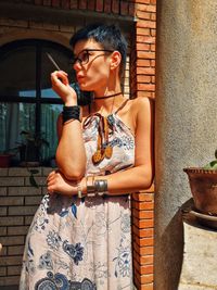 Portrait of young woman wearing sunglasses standing against wall