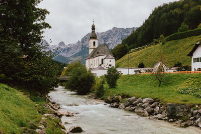 Stream amidst trees and buildings against sky
