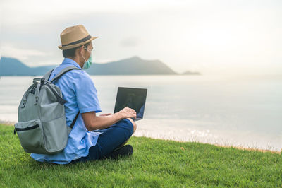 Rear view of man using laptop while sitting on field