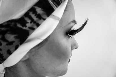 Profile view of young woman with false eyelash against white background