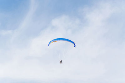 Low angle view of person paragliding against cloudy sky on sunny day