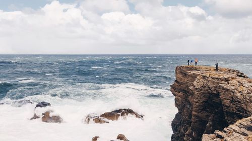 Friends standing on cliff against sea at beach