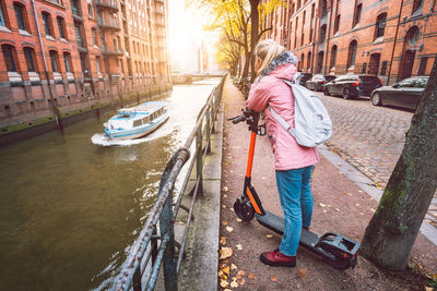 Rear view of woman with push scooter on footpath