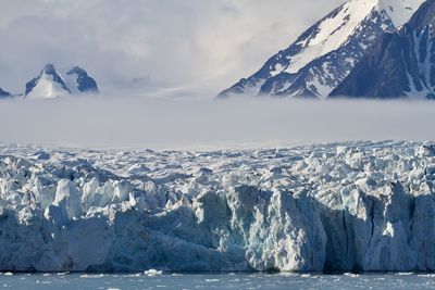 A low cloud hangs above an arctic glacier where it meets its fjord