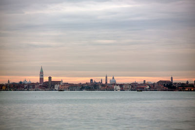 River by buildings in city against sky during sunset