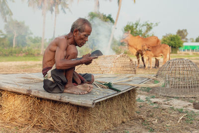 Shirtless senior man making straw basket