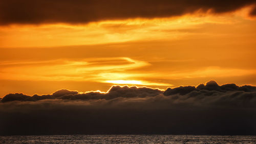 Scenic view of sea against dramatic sky during sunset