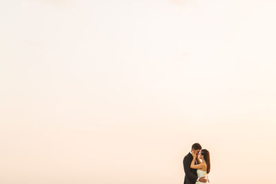 Couple kissing against clear sky during sunset