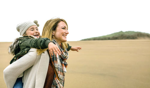 Happy woman carrying daughter piggyback on the beach in winter