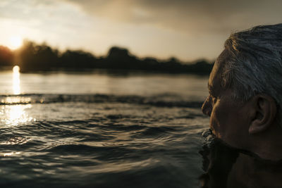 Senior man swimming in a lake at sunset