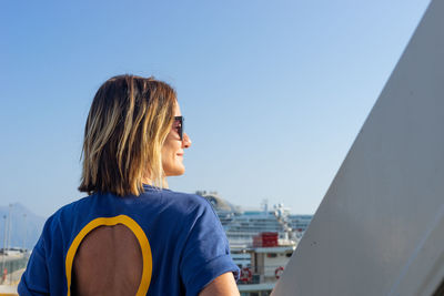 Rear view of woman wearing sunglasses standing against clear sky