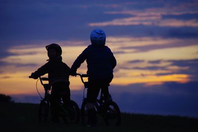 Father and son on field against sky during sunset