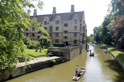 People on river amidst trees and buildings