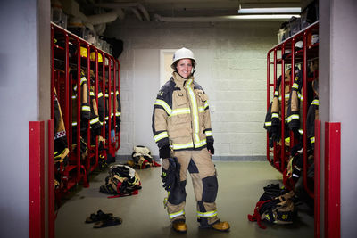 Full length portrait of smiling female firefighter standing in locker room at fire station