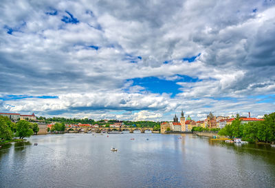 View of buildings by river against cloudy sky