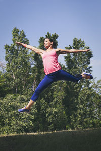 Low angle view of woman jumping against trees