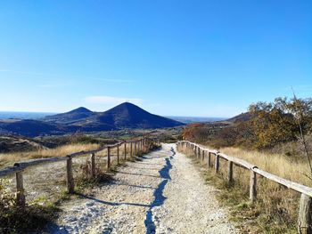 Road leading towards mountain against clear blue sky
