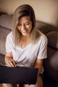 Portrait of young woman using laptop while sitting on sofa at home