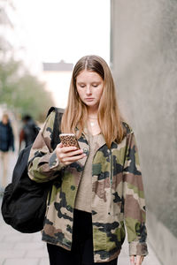 Teenage girl in camouflage shirt using smart phone while walking on footpath