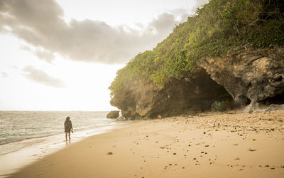 Rear view of woman walking on beach against sky