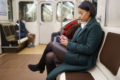 Unhappy tired african woman surfing social media in smartphone ride subway metro home from work