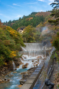 Scenic view of waterfall by trees against sky